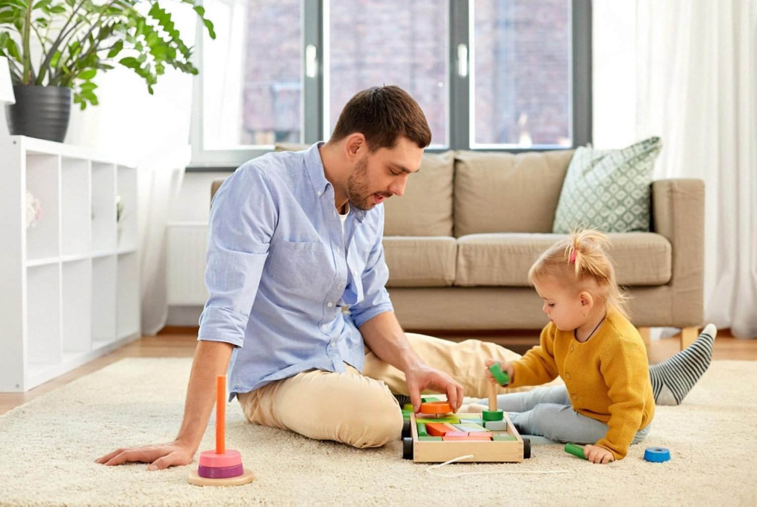 Father and toddler in a Dubai living room playing with wooden stacking and shape-sorting toys for independent learning