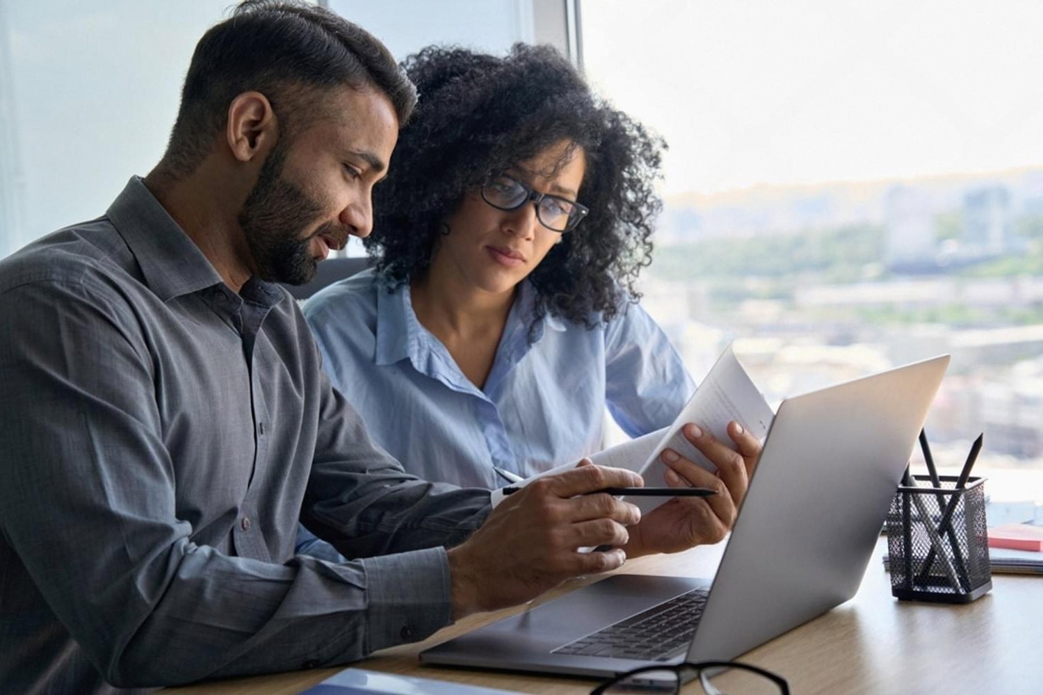 Compliance officer and analyst reviewing customer due diligence files on a laptop in a Dubai office