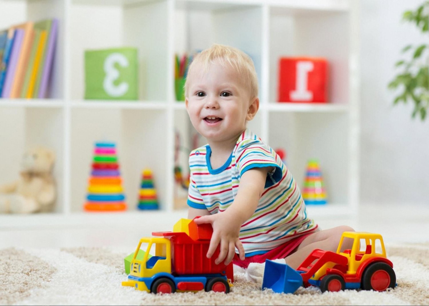 Young child in the UAE smiling while playing alone with colourful learning toys and stacking rings